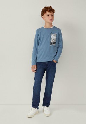 Blaues Longsleeve-T-Shirt mit Grafikdruck auf der Vorderseite, kombiniert mit dunkelblauen Jeans und weißen Sneakern. Schlichte, lässige Passform.