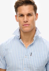Kortegestreepte lichtblauwe shirt met korte mouwen en een button-down kraag, met een borstzak en een klein logo-label aan de voorkant.