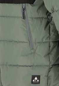 Puffjacka i ljusgrön med svarts yoke, har en ficka med dragkedja, quiltad textur och en svart logotypficka nere till höger.