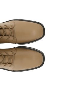 Beżowe skórzane buty o gładkiej fakturze, okrągłym nosku i płaskiej czarnej gumowej podeszwie. Posiadają pasujące sznurówki i minimalistyczny design.