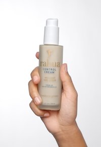 In einer frostigen beige-farbenen Flasche mit weißer Pumpe befindet sich flüssige Anti-Frizz-Lockencreme, die goldene und blaue Schriftzüge aufweist und in einer Hand gehalten wird. 120 ml.