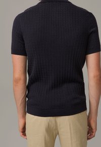 Polo shirt bleu marine à manches courtes à côtes avec une coupe ajustée, en tissu texturé, et un col uni. L'ourlet du vêtement est fini avec une bande sombre.