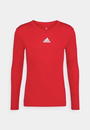 Maglietta sportiva rossa a maniche lunghe realizzata in tessuto liscio e elasticizzato. Presenta un collo a V e il logo Adidas bianco sul petto.