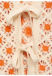 Háčkovaný vzor s květinovým motivem oranžových a bílých květin, svázaný slonovinovým šňůrkem. Texturovaná, otevřená tkanina.
