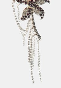 Spilla floreale argentata con strass rosso scuro e trasparenti, caratterizzata da catene pendenti di diverse trame e lunghezze.