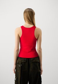 Débardeur rouge à côtes avec un col rond et des bretelles larges, associé à un pantalon cargo noir avec des poches latérales. Texture lisse et design ajusté.