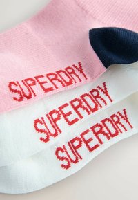 Skarpetki w kolorze różowym, białym i granatowym; każda z nich posiada haftowane słowo "SUPERDRY" w kolorze czerwonym. Strukturalna bawełniana tkanina i wysokość do kostki.