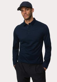Navyblaues Langarm-Polohemd mit Kragen, ausgestattet mit einer Knopfleiste mit drei Knöpfen und einer glatten Stoffstruktur. Kombiniert mit dunklen Hosen und einer passenden Mütze.