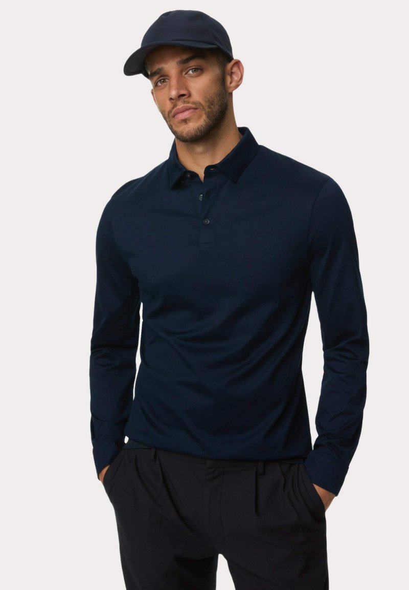Navyblaues Langarm-Polohemd mit Kragen, ausgestattet mit einer Knopfleiste mit drei Knöpfen und einer glatten Stoffstruktur. Kombiniert mit dunklen Hosen und einer passenden Mütze.