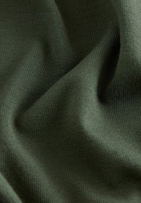 Olivgrüner gestrickter Stoff mit glatter Textur, der sanfte Falten zeigt und ein gleichmäßiges geripptes Muster aufweist.