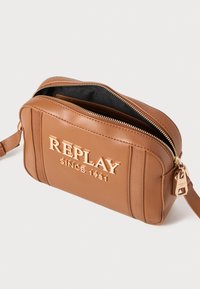 Brun skinn crossoverveske med preget "REPLAY SINCE 1981" logo, gull aksenter, glidelås forsegling og justerbar stropp.