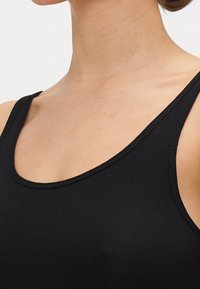 Musta hihaton toppi paksuilla olkaimilla, pyöreällä kaula-aukolla ja sileällä, kevyellä kankaalla. Ominaisuuksiin kuuluu vartaloa myötäilevä muotoilu ja minimaalinen ompelutaito.