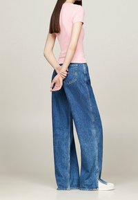 Light pink fitted t-shirt paired with high-waisted, wide-leg blue denim jeans featuring side slits, worn with white sneakers.