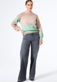 Gebreide trui met een geometrisch patroon, dat overgaat van lichtroze naar mintgroen, gecombineerd met hoog-waist, wijde donkerblauwe jeans.