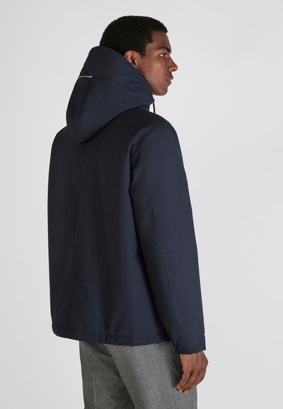Navy hooded jacket with a smooth texture, elastic cuffs, and a subtle rear accent at the neckline. The design is boxy and casual.