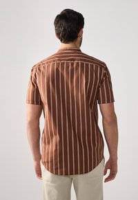 Brown short-sleeve shirt with white vertical stripes, featuring a button-down collar and a curved hem, made from a textured fabric.