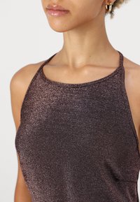 Top halter metálico marrón con una textura suave, diseño ajustado y un escote sencillo. Las tirantes son finas y ajustables.