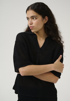 Black short-sleeve top with a V-neck, made of textured mesh fabric. Features a flat collar and a relaxed fit, with an overlapping hemline design.
