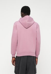 Φούτερ με κουκούλα σε απαλή ανοιχτό ροζ απόχρωση. Διαθέτει ριμπ μανσέτες και στρίφωμα, χαλαρή εφαρμογή και σχεδίαση κουκούλας χωρίς ραφές. Μινιμαλιστικό στυλ χωρίς διακοσμητικά στοιχεία.