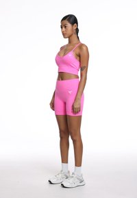 Jasnoróżowy zestaw sportowy składający się z krótko skrojonym topem na ramionach i szortami z wysokim stanem, wykonany z rozciągliwego materiału o teksturowanym wykończeniu, w zestawieniu z białymi trampkami.