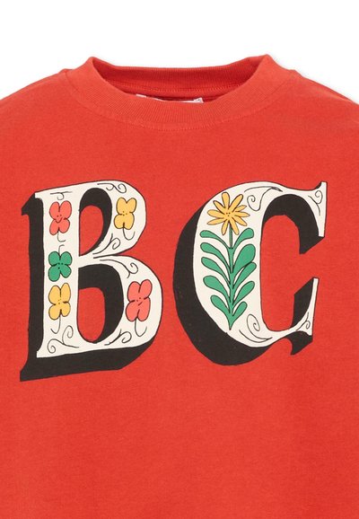 Vêtement rouge avec de grandes lettres blanches "B" et "C" décorées de fleurs colorées et de feuilles vertes, doté d'un col rond.