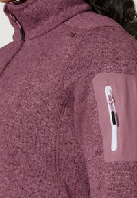 Sopiva, korkea kauluksellinen fleece-takki tummanoranssina, jossa on teksturoitu kangas. Varustettu vetoketjullisella hihapussilla ja kontrastivärisellä sileällä paneelilla.