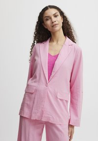 Light pink linen blazer with notch lapels, two front pockets, and a single button closure. Worn over a pink knitted top. Smooth texture.