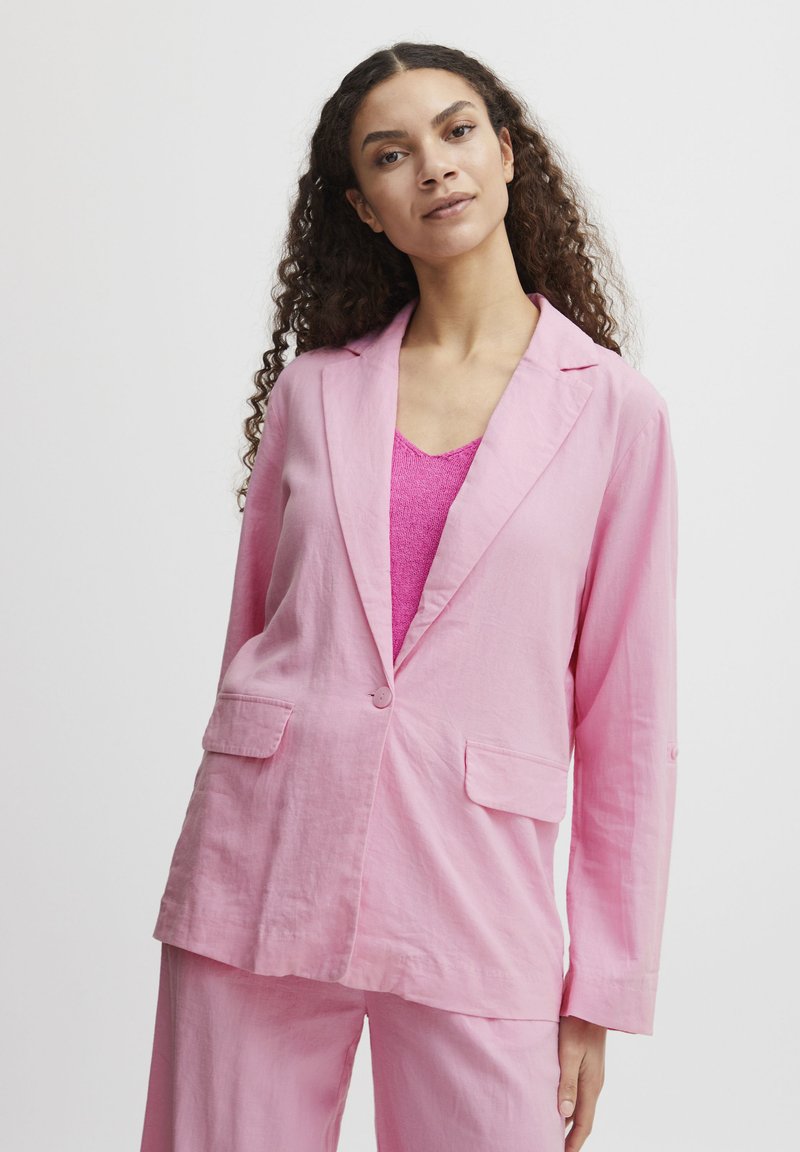 Light pink linen blazer with notch lapels, two front pockets, and a single button closure. Worn over a pink knitted top. Smooth texture.