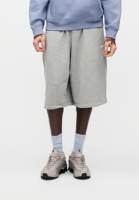 Γκρι βαμβακερά σορτς με πλαϊνές τσέπες, συνδυασμένα με ανοιχτό μπλε καλτσάκια μέχρι τον αστράγαλο και μπεζ αθλητικά παπούτσια με χαρακτηριστικό σχέδιο σόλας.