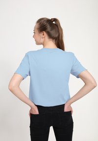 T-shirt di cotone azzurro chiaro con maniche corte e collo tondo, indossata con jeans di denim neri, che mostra un design semplice e casual.