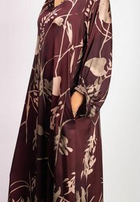 Burgundyklänning med botaniska tryck i beige. Har en lös passform, korta ärmar och sidofickor. Tillverkad av lättviktigt tyg.