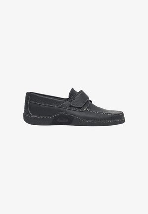 Mocasín negro de cuero con tira de velcro, costuras en contraste y suela con textura, diseñado para comodidad al calzar y uso informal.