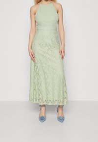 Mintgrön maxiklänning med halterneck, spetsöverdrag och figurnära överdel. Matchas med högklackade skor prydda med blå rosor.