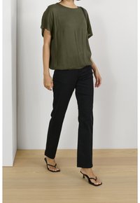 Top oversize verde oliva in tessuto leggero, abbinato a pantaloni neri a gamba dritta e sandali con tacco a infradito neri. Design semplice.