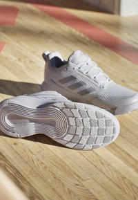 White athletic shoes featuring a textured mesh upper, three gray stripes, and a rubber sole with a patterned tread for traction.
