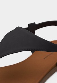 Μαύρο δερμάτινο σανδάλι με φαρδιά λουρί πάνω από τη δερμάτινη σόλα σε ταμπά απόχρωση και ρυθμιζόμενο λουρί στον αστράγαλο, κοντινή όψη.