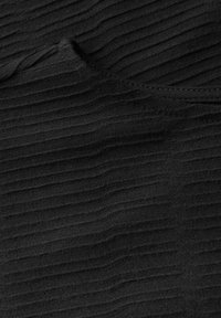 Svart texturerad tyg med horisontella åsar. Materialet är något elastiskt, med släta kanter och en rund halsringning.