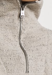 Pull gris clair avec un col montant et une fermeture éclair en métal. Motif de tricot texturé avec de petites nuances discrètes.