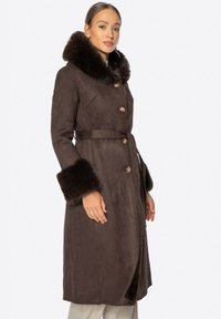 Brązowy płaszcz z futrzanym wykończeniem, z kołnierzem i mankietami, podwójnie zapinany na złote guziki, z paskiem w talii i miękką, zamszową teksturą.