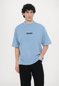 Kék, rövid ujjú póló pamut keverékből, kerek nyakkal, a hónaljba helyezett középen fekete logóval, amelyen az "MICHAEL KORS" felirat szerepel.