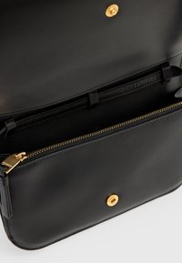 Schwarze Lederhandtasche mit goldenen Beschlägen im Inneren. Verfügt über eine Reißverschlusstasche und Kartenfächer zur Organisation. Glatte Textur, minimalistisches Design.