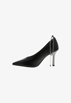 Chaussure à talon aiguille noire à bout pointu avec un talon stiletto argenté et un accessoire en chaîne argentée pendent au dos.
