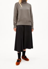 Pull en maille gris à col roulé, jupe midi noire, chaussettes noires et chaussures en velours orange avec une bride, créant une tenue superposée.