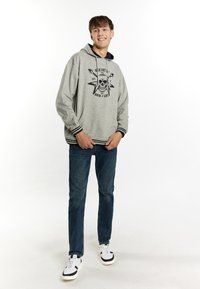 Felpa grigia con cappuccio, grafica di teschio e chitarra nera, lacci neri e polsini a righe. Abbinata a jeans in denim scuro e sneakers.