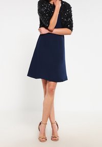 Syvänsininen mekko, jossa on kiinnitetty siluetti ja lyhyt musta paljettibolero. Ominaisuuksina sileä pinta ja kultaiset nilkkaketjusaappaat.