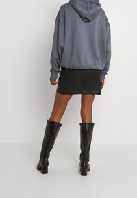 Grå oversized hoodie, svart läder minikjol och knähöga svarta lackstövlar med krokodilstruktur. Rena linjer och minimalt med detaljer.