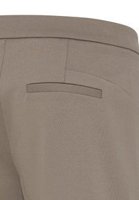 Gros plan sur un pantalon en tissu beige montrant une poche passepoilée arrière avec des coutures propres et une ceinture lisse.