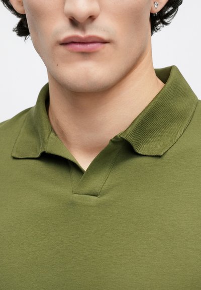 Olivzaļš polo krekls ar fakturētu audumu, klassiska apkakle un V veida plāksne. Tuvplāns, minimālistisks dizains.
