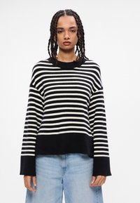 Suéter de malha riscado em preto e branco com um corte descontraído, decote redondo e mangas longas, combinado com jeans de perna larga em azul claro.