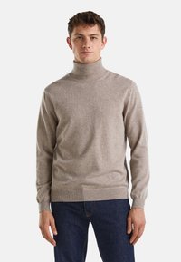 Maglione a collo alto beige chiaro realizzato in materiale morbido, con maniche lunghe e una vestibilità aderente, abbinato a jeans in denim scuro.